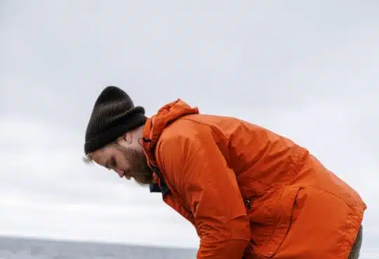 Man in Orange Jacket and Blue Denim Jeans Standing on Water